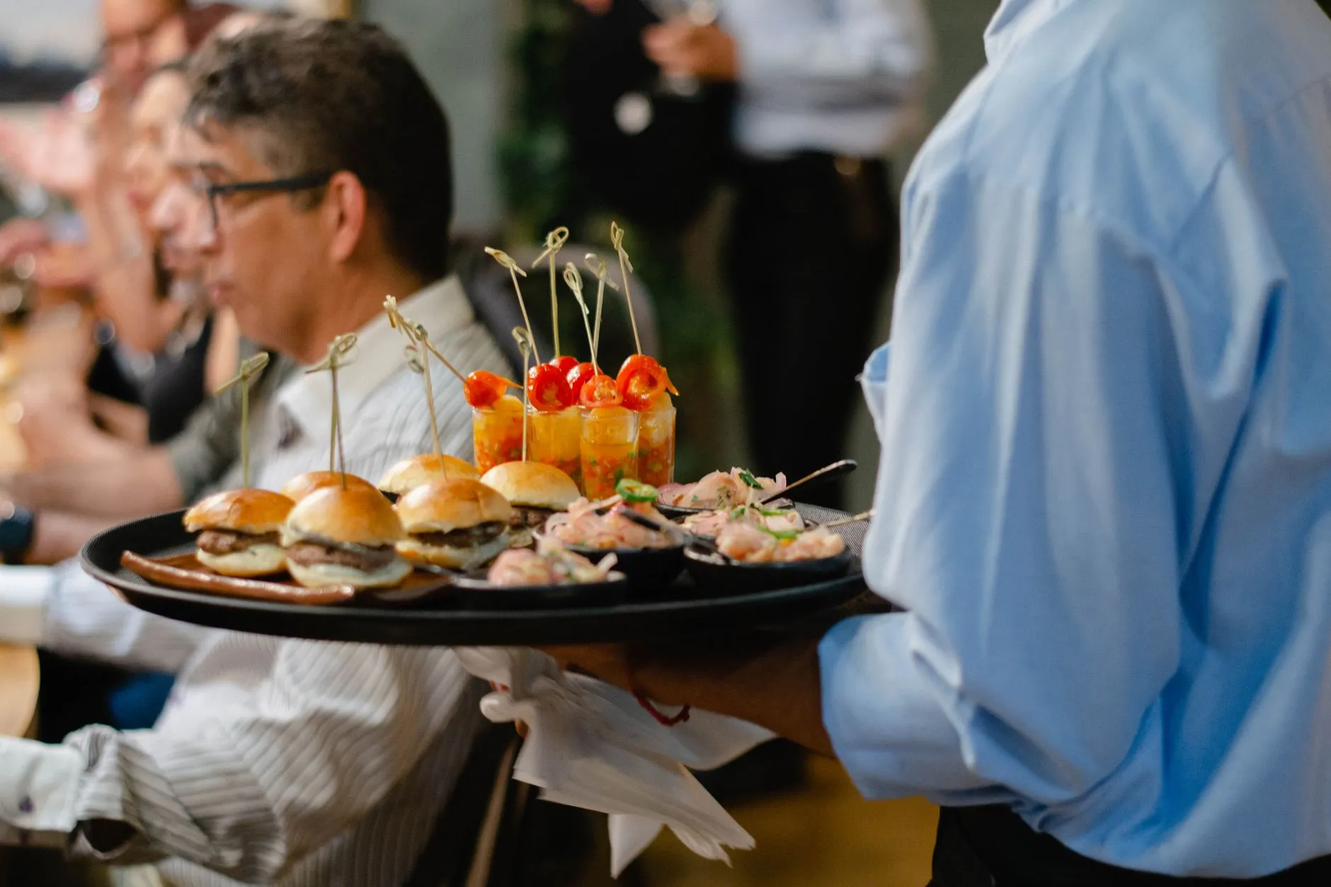 Garçom freelancer servindo canapés em bandeja para convidados de um evento