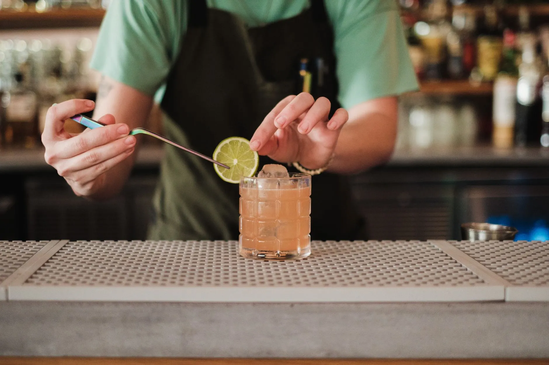 Bartender finalizando um drink com uma rodela de limão no balcão de um bar